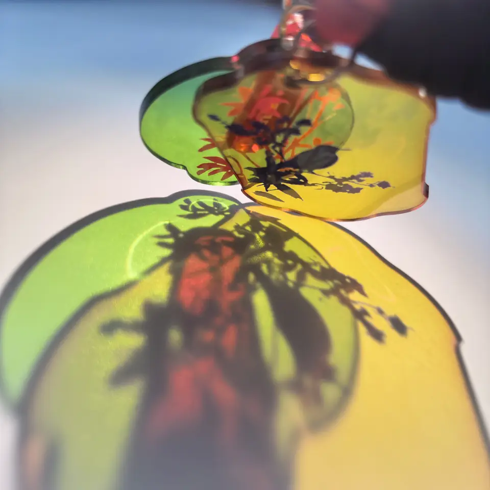 RETLPER translucent floral and bird acrylic keychain casting green and yellow shadows in sunlight