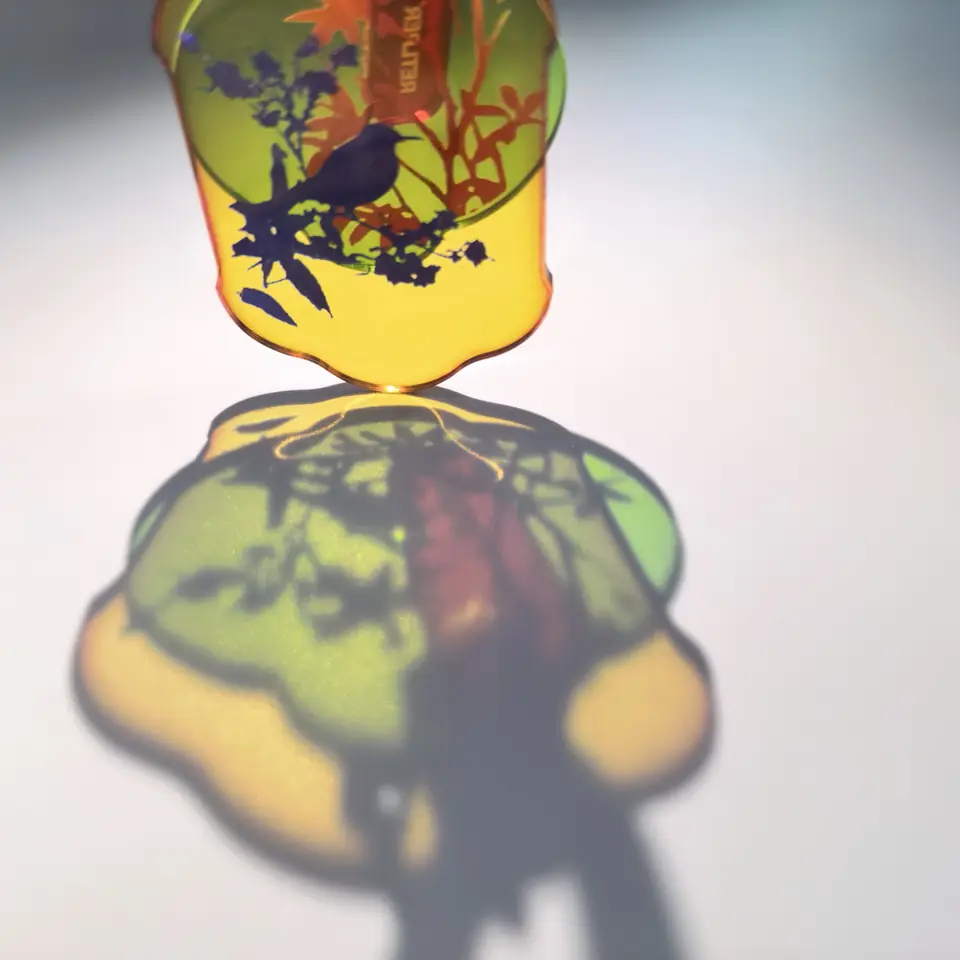 Close-up of yellow bird and green floral acrylic plaques casting colorful patterned shadows