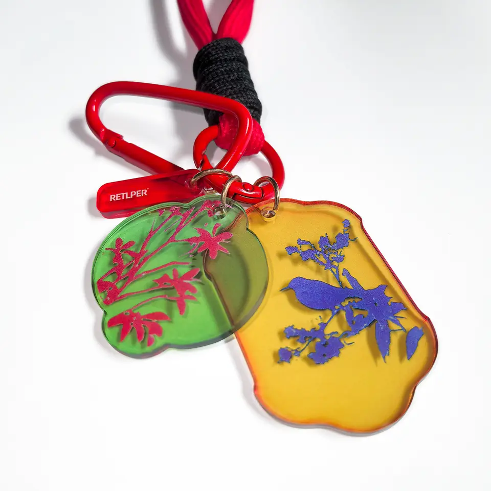Close-up of RETLPER green floral and yellow bird acrylic plaques with red clip and brand tag