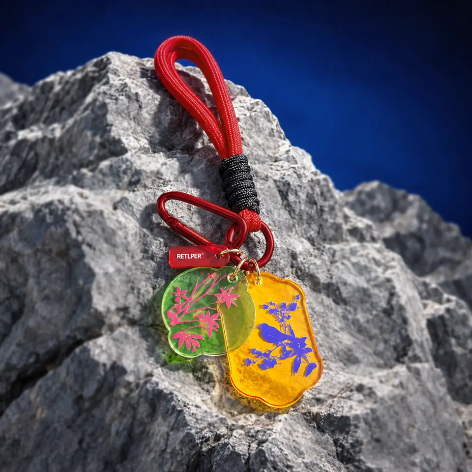 RETLPER acrylic keychain with red strap, green floral plaque and yellow bird plaque on a rock